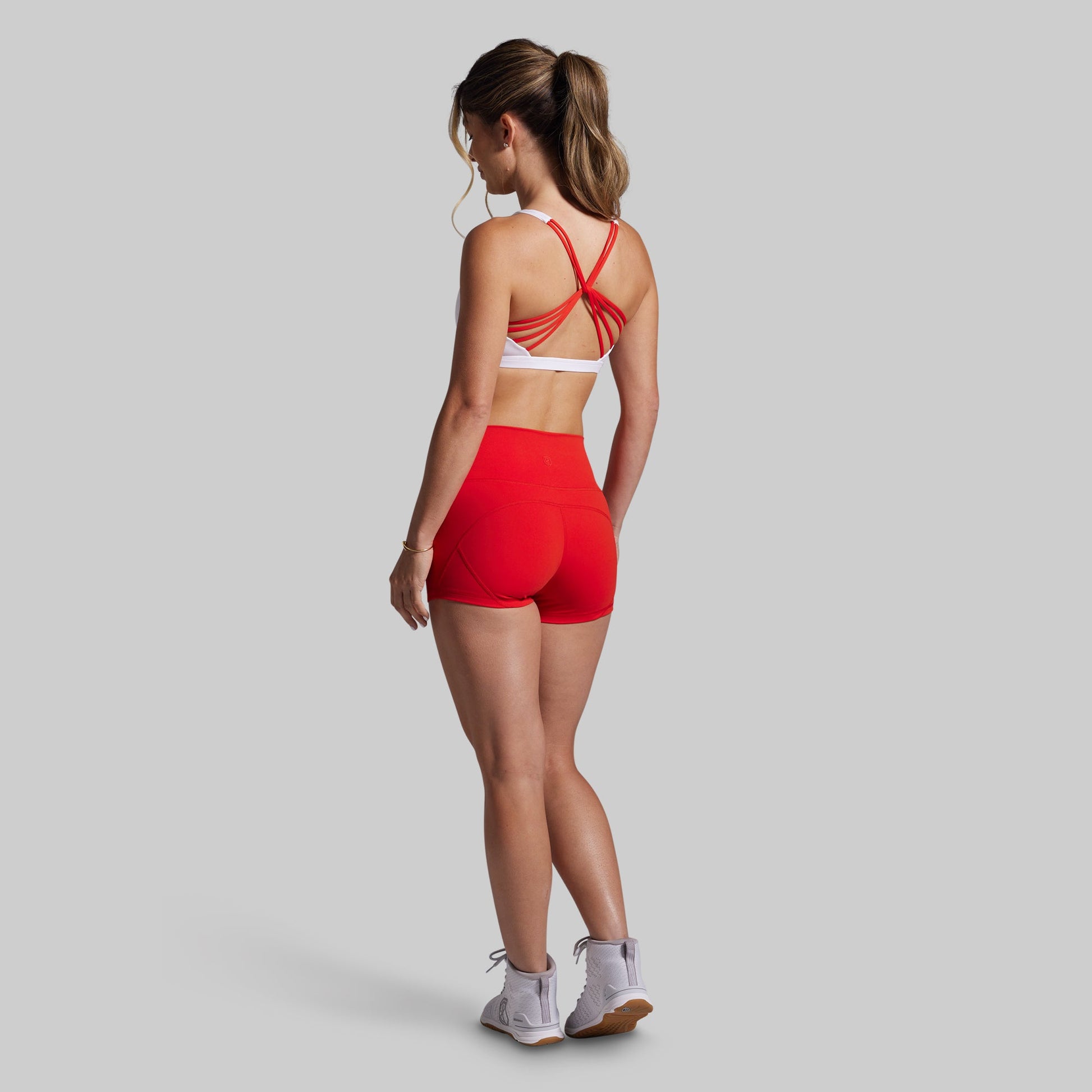 Woman wearing a white sports bra with red straps and shorts on a gray background
