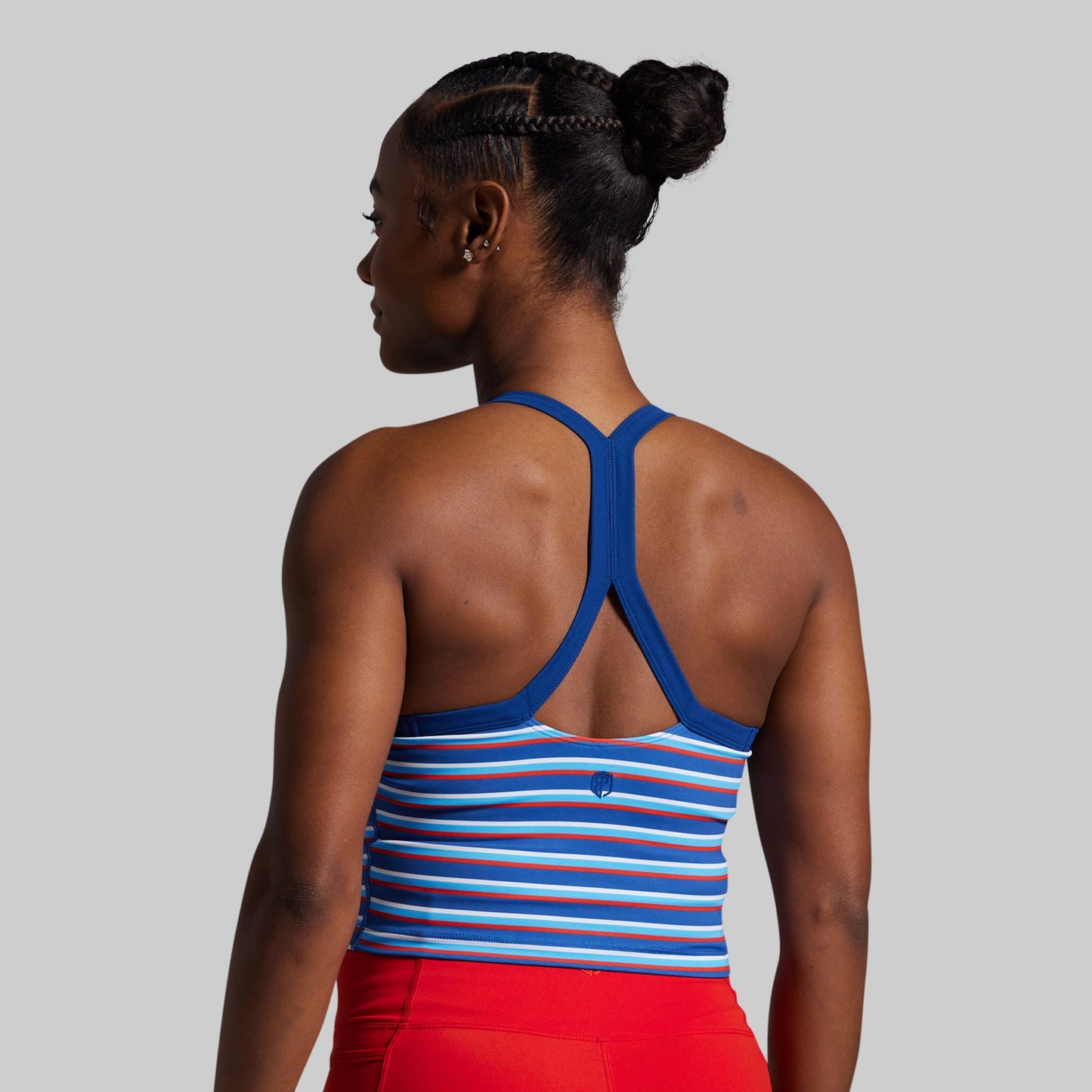 Woman wearing a blue and white striped sports bra with red shorts on a gray background