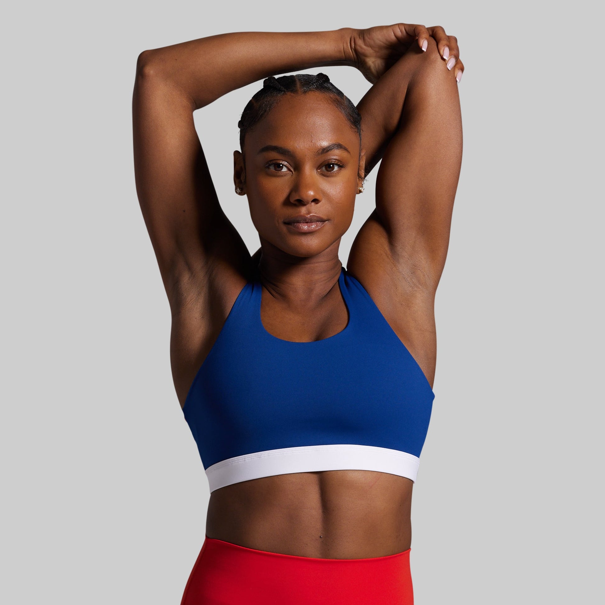 Woman wearing a blue sports bra and red leggings on a gray background