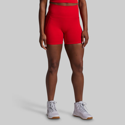 Person wearing red athletic shorts and white sneakers on a gray background