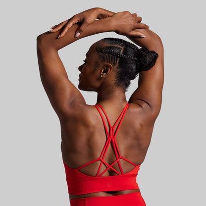 Woman wearing a red sports bra with criss-cross straps on a gray background