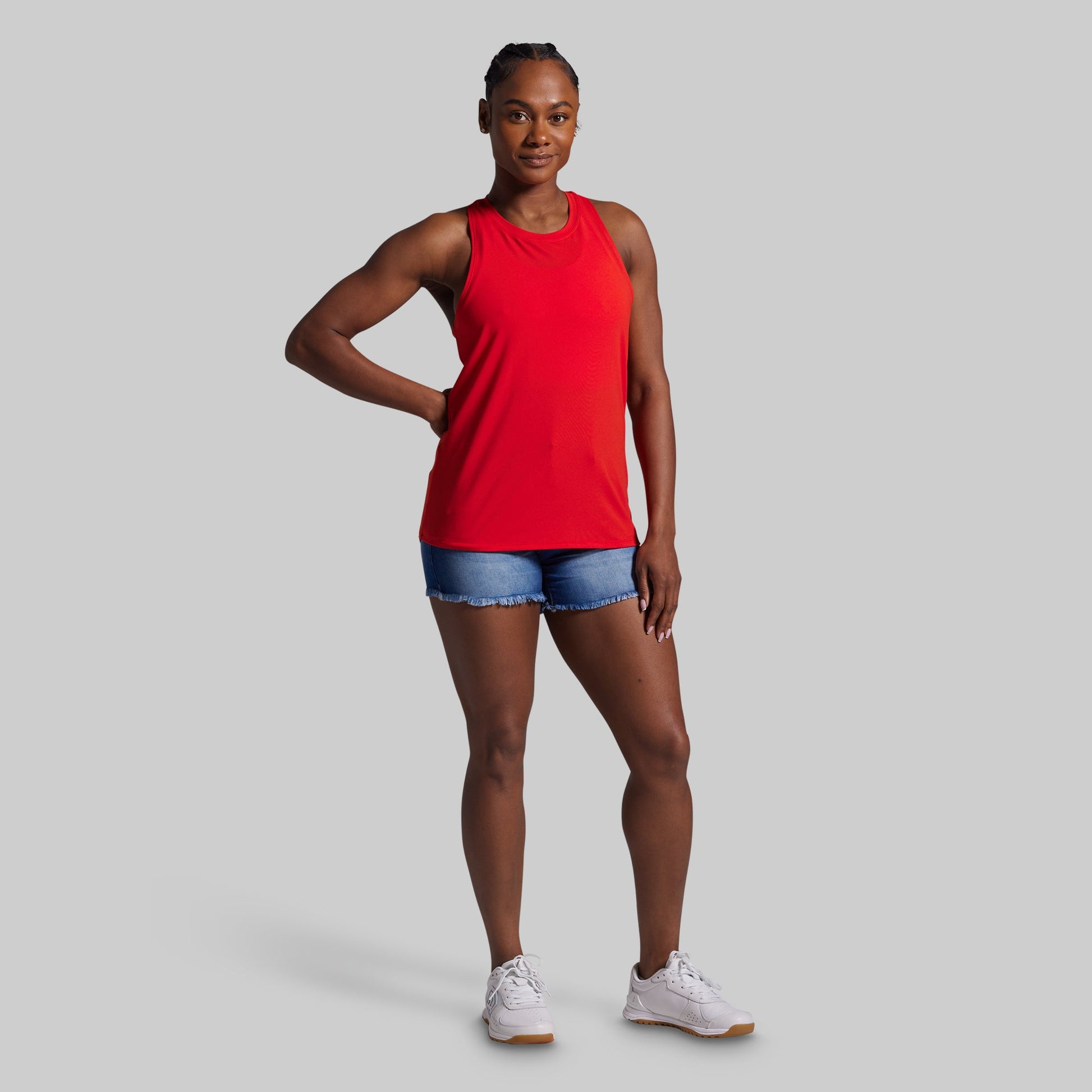 Woman wearing a red tank top and denim shorts on a gray background
