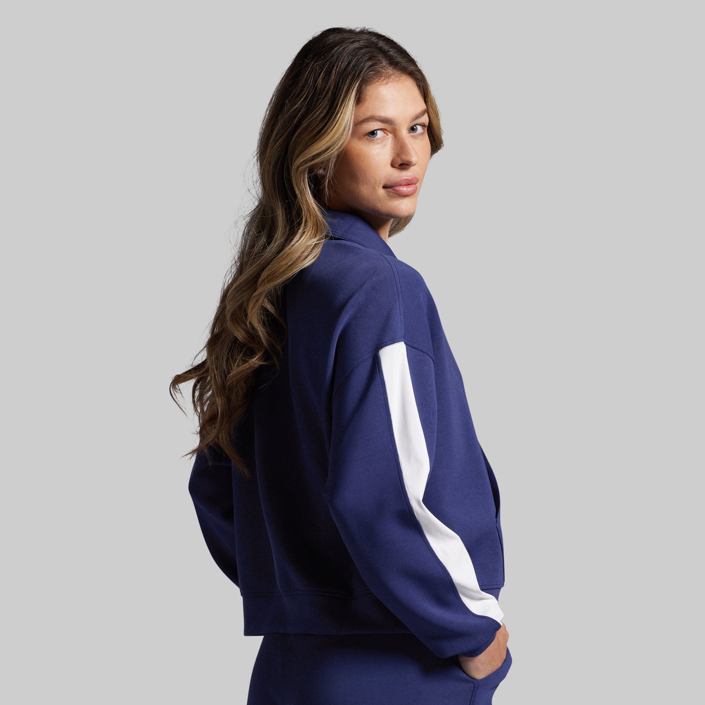 Woman wearing a navy blue sweatshirt with a white stripe on a gray background