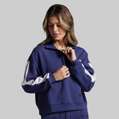 Woman wearing a blue sweatshirt with white accents on a gray background