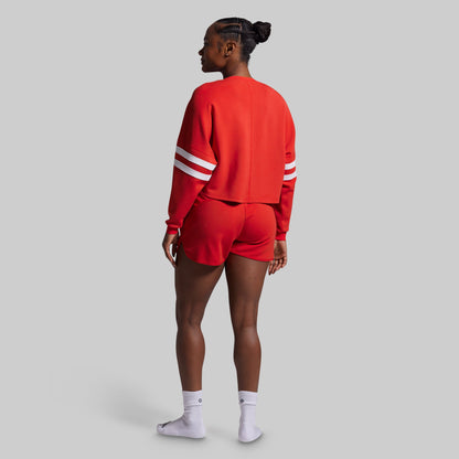 Person wearing a red sweatshirt with white stripes and shorts on a gray background