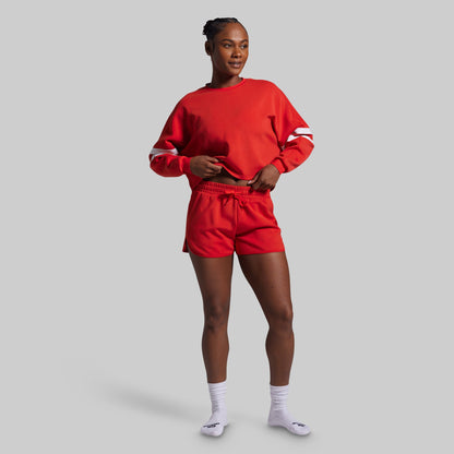 Person wearing a red sweatshirt and shorts on a gray background
