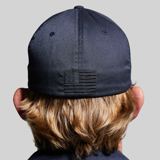 Person wearing a navy blue cap with an American flag patch on a gray background