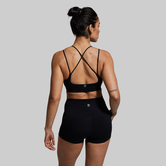 Woman wearing a black sports bra with criss-cross straps on a gray background