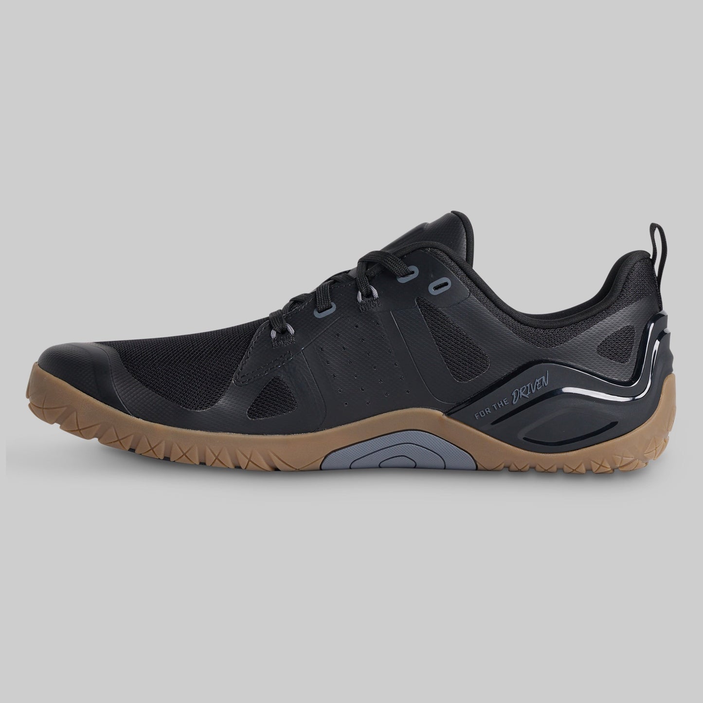 A black athletic shoe with a brown gum sole, shown in a side profile view against a solid gray background.