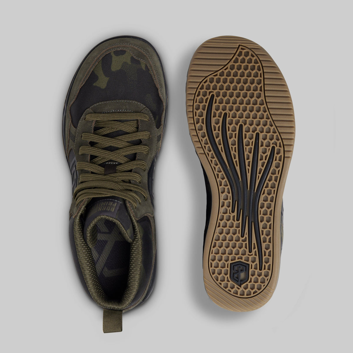 A pair of mid-top sneakers shown from the top and bottom views against a light gray background. The upper is dark camouflage in black and olive green, with matching green laces and a pull tab.