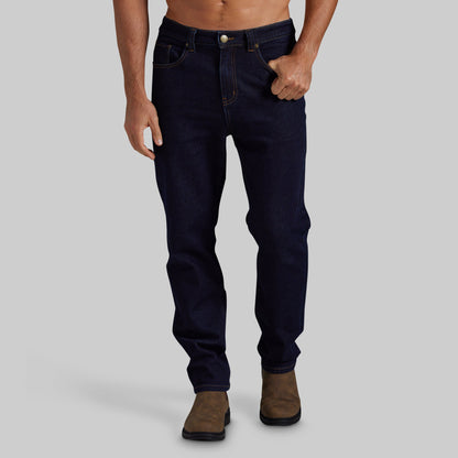 A man wearing dark navy blue slim-fit jeans and brown boots, shown from the waist down against a solid gray background.