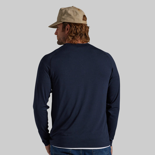 A man wearing a navy blue long-sleeve shirt and a beige baseball cap, shown from the back against a solid gray background.