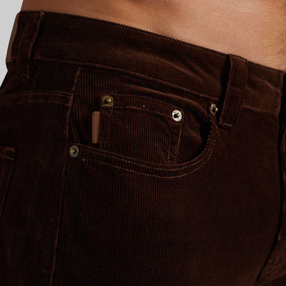 Close-up of a person wearing dark brown corduroy pants, showing the front pocket and waistband area.