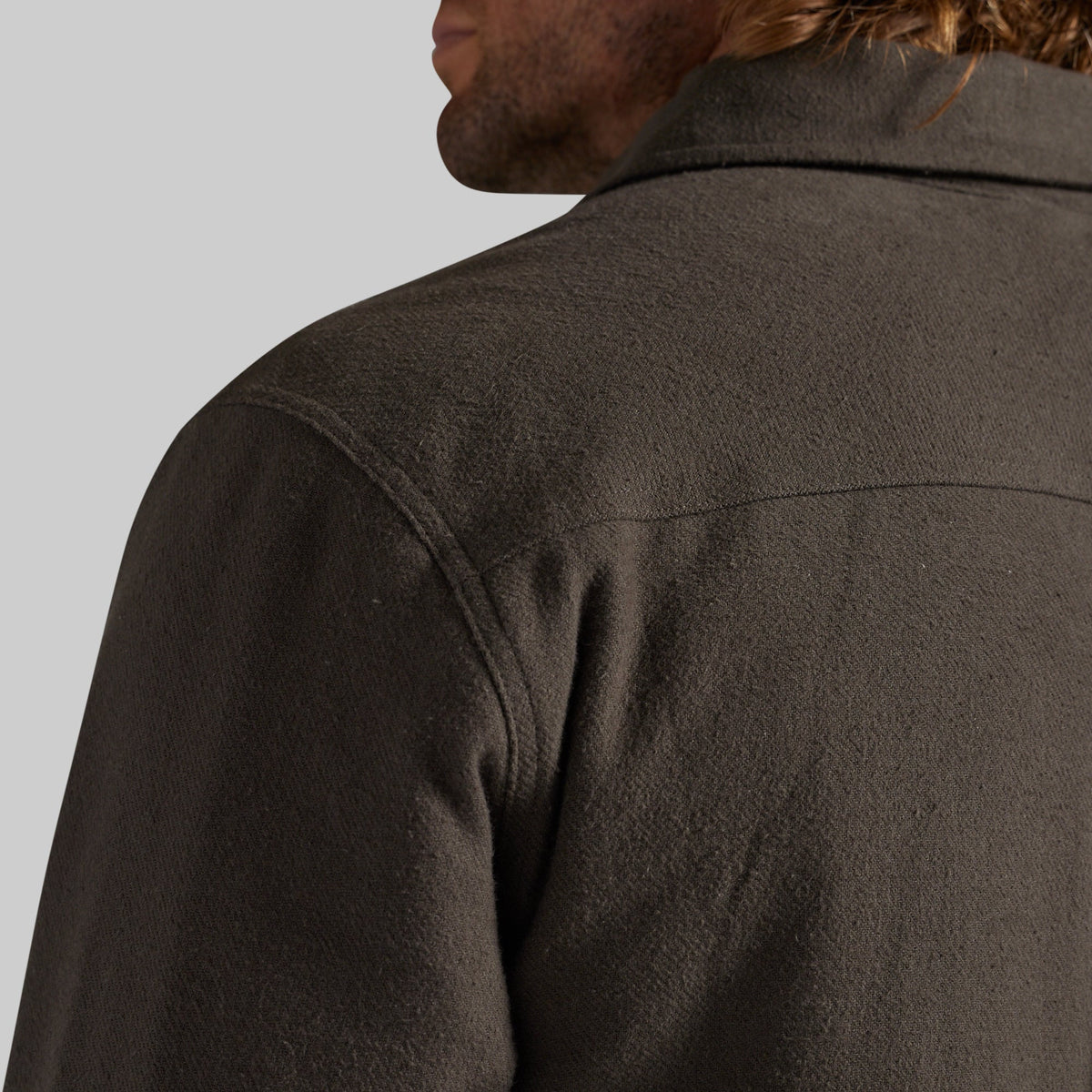 Close-up back view of a person wearing a dark brown textured jacket against a light gray background.