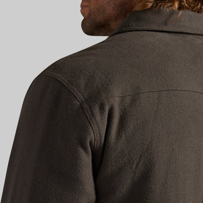 Close-up back view of a person wearing a dark brown textured jacket against a light gray background.