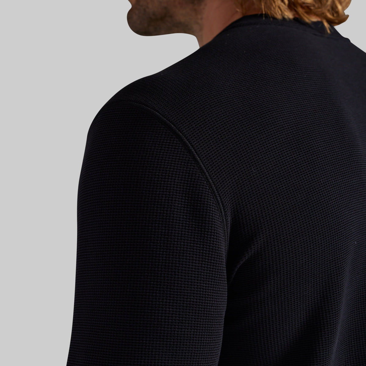 Close-up back view of a man wearing a black textured knit crewneck sweater against a light gray background.