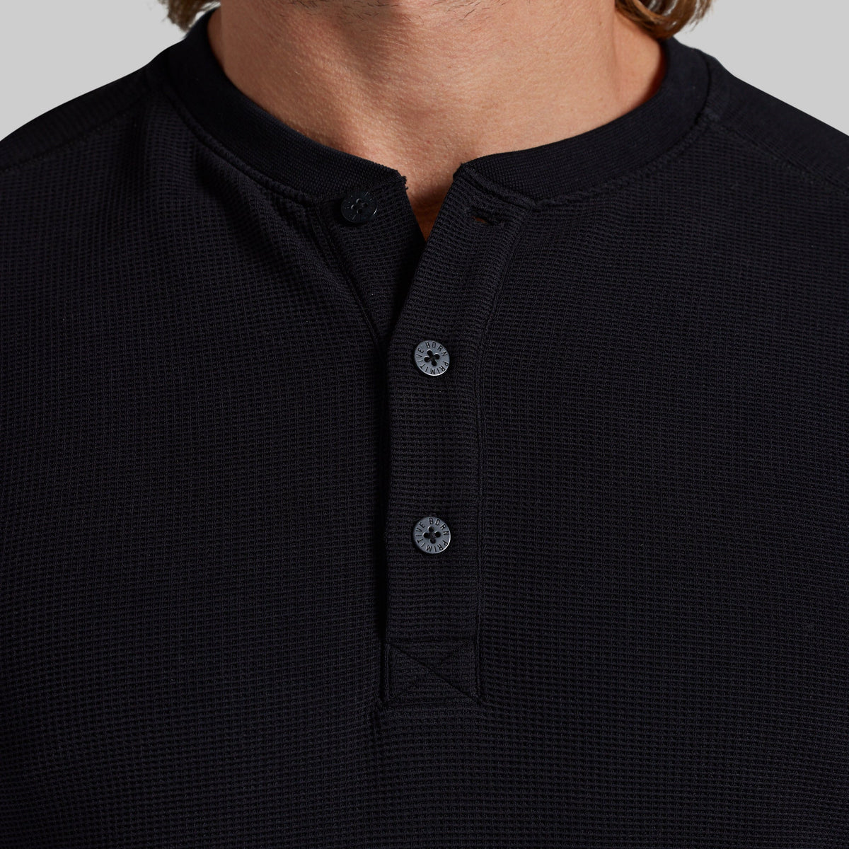 Close-up of a person wearing a black waffle-knit henley shirt with a button placket and a short stand collar.
