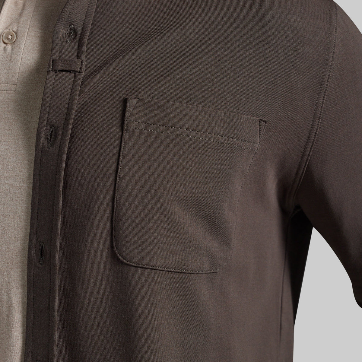 Close-up of a dark olive brown overshirt worn over a light beige polo shirt, highlighting chest pocket
