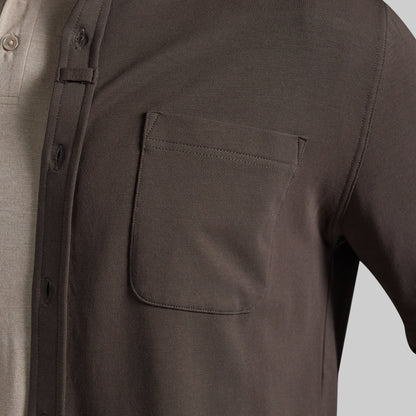 Close-up of a dark olive brown overshirt worn over a light beige polo shirt, highlighting chest pocket