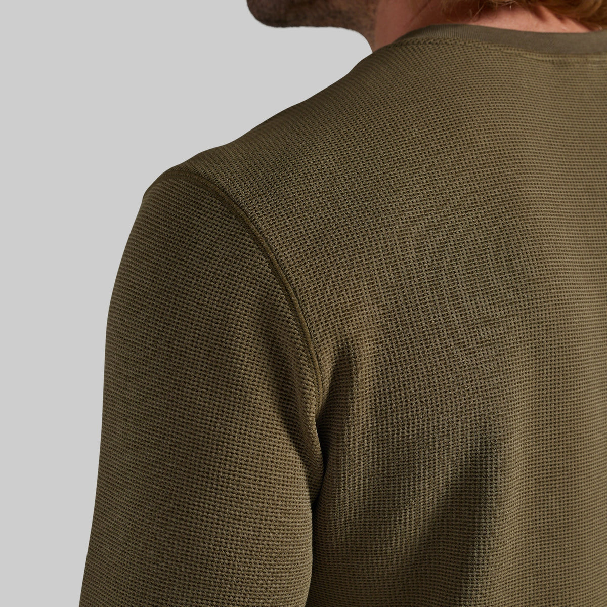 Close-up of a man wearing a textured olive green long-sleeve shirt, showing the waffle-knit fabric and shoulder detail against a neutral gray background.