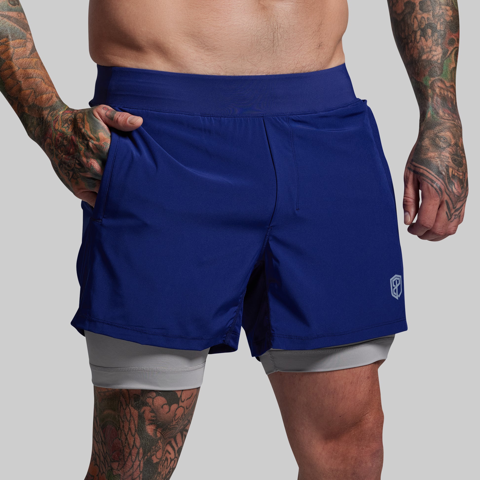 Person wearing blue athletic shorts with a small logo on a gray background