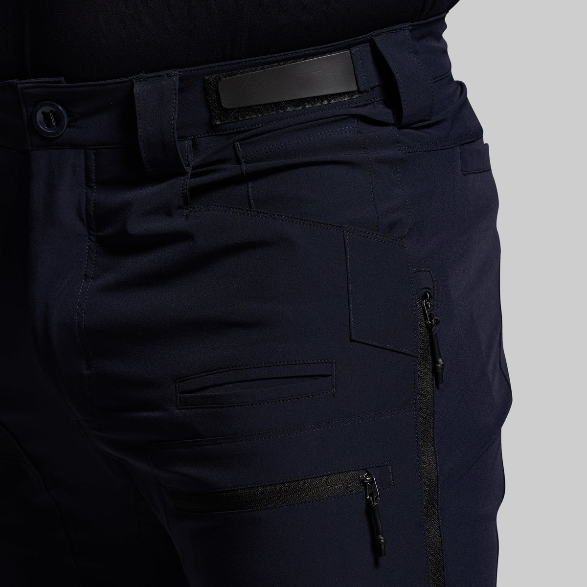 Navy blue outdoor pants with multiple pockets and zippers on a gray background