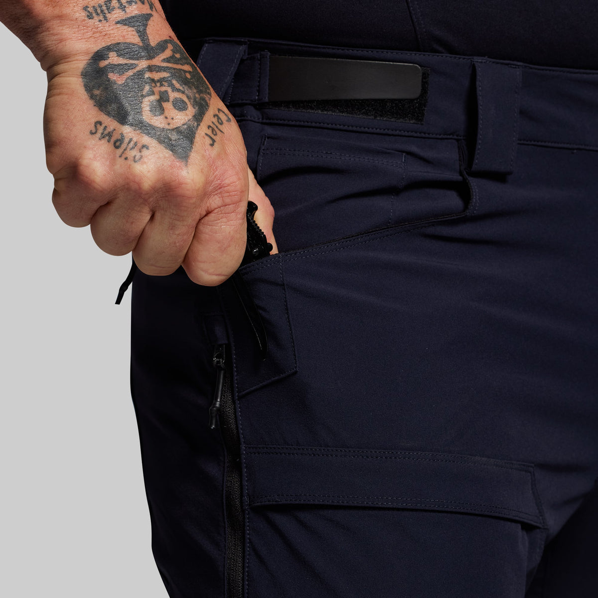 Person wearing dark blue outdoor pants with a tattooed hand on a gray background