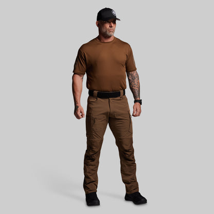 Man wearing a brown t-shirt and pants with a black cap on a gray background