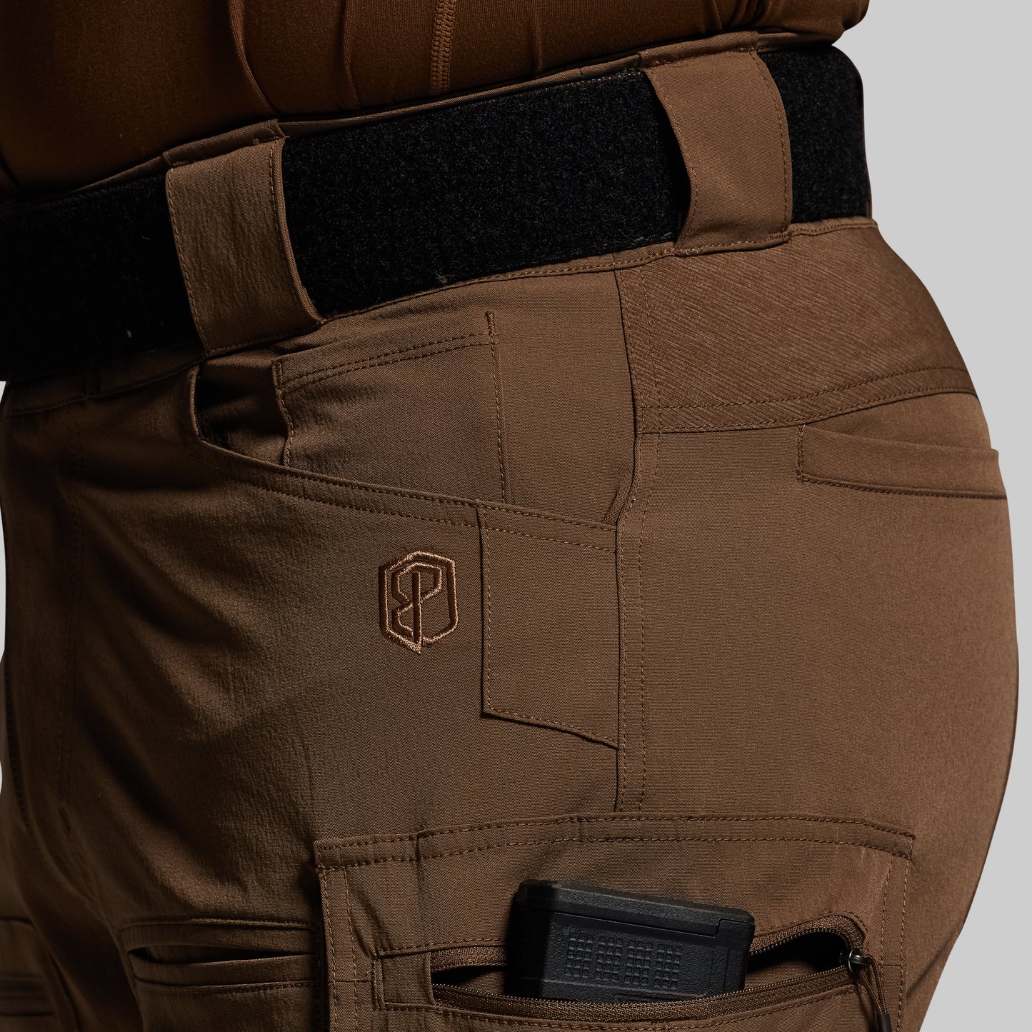 Brown tactical pants with a visible brand logo on a gray background