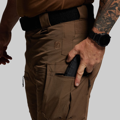 Person wearing brown tactical pants with a visible brand logo, holding a magazine.