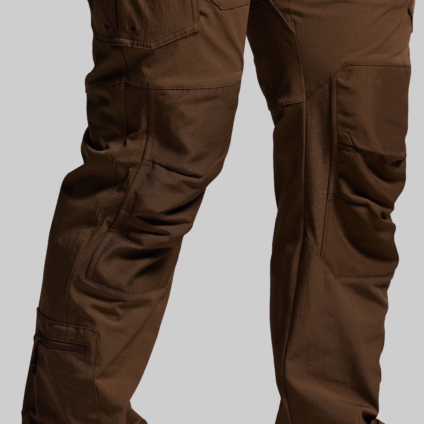 Close up of reinforced knees on brown tactical pants on a light gray background