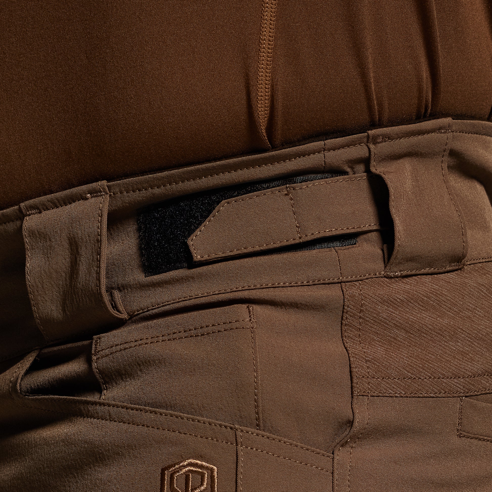 Close-up of brown tactical pants with a visible brand logo.