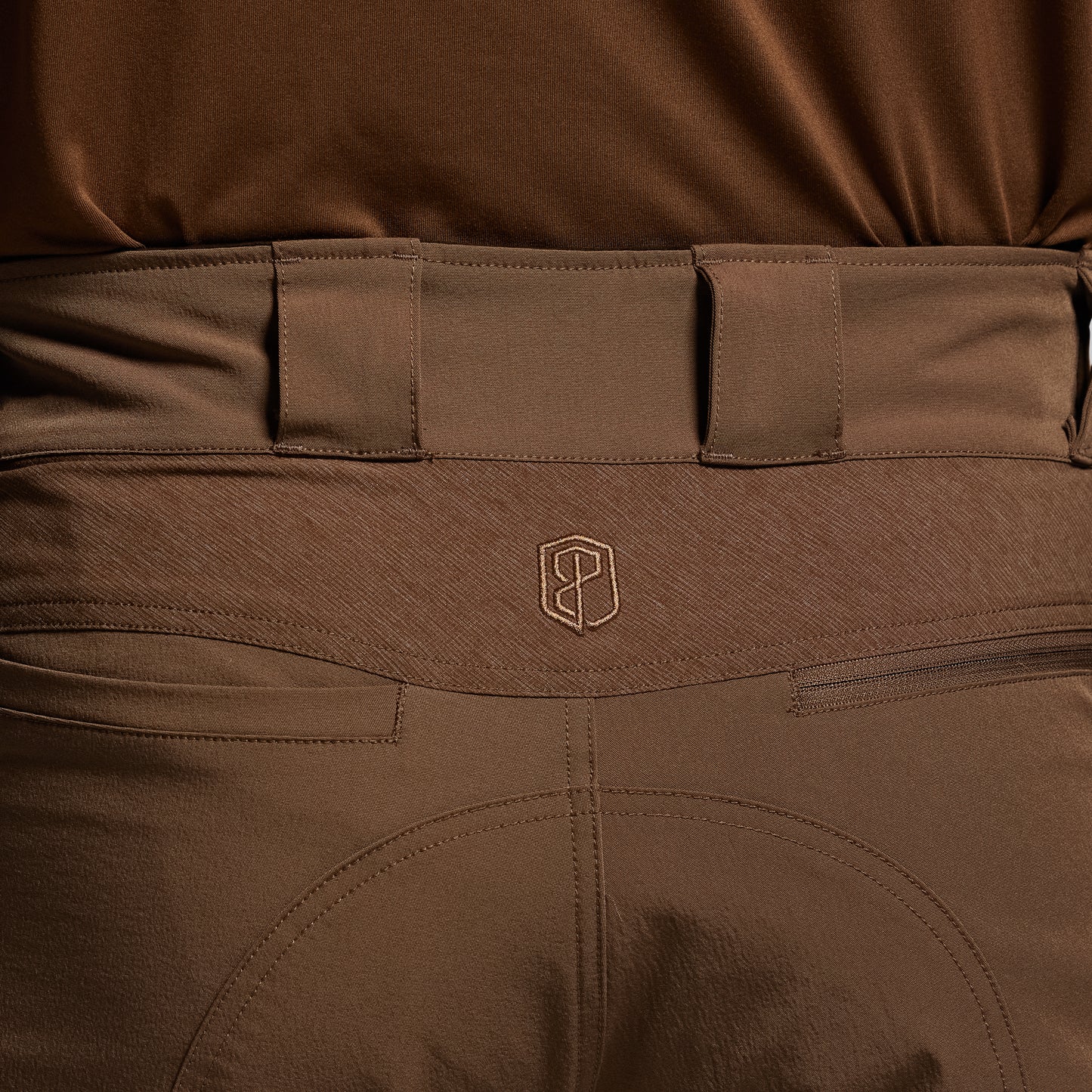 Close-up of brown tactical pants with a visible brand logo on the waistband.