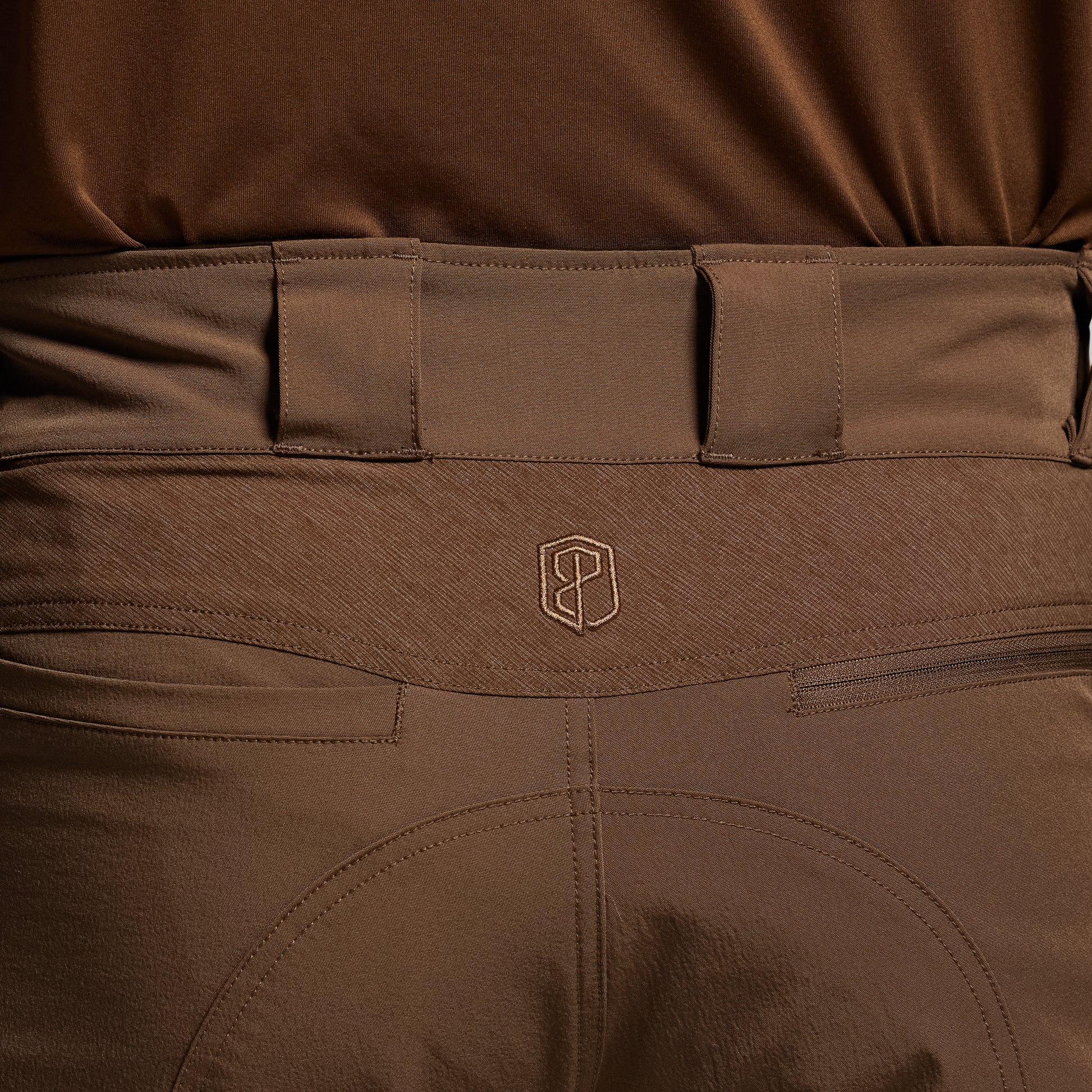 Close-up of brown tactical pants with a visible brand logo on the waistband.