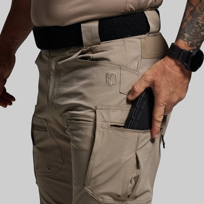 Person wearing beige tactical pants with a visible brand logo, holding a black object.