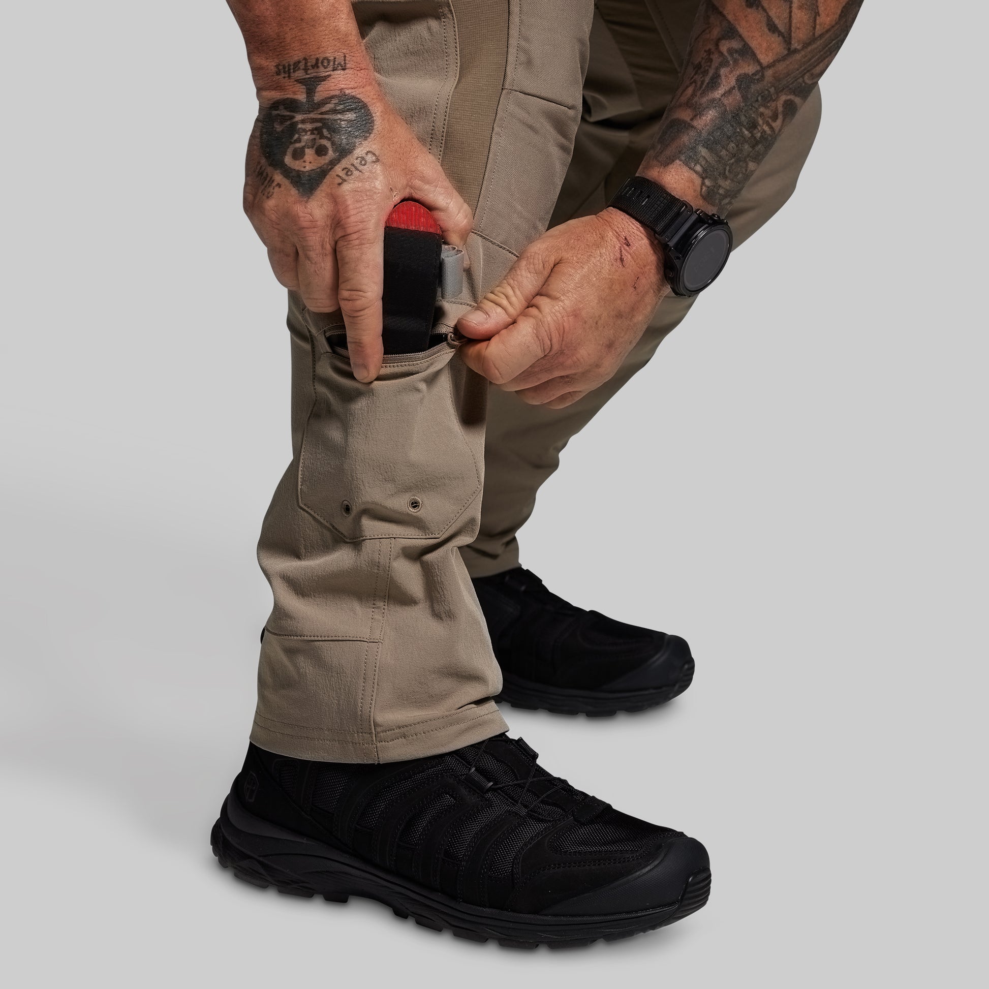 Person wearing beige pants and black shoes on a plain background