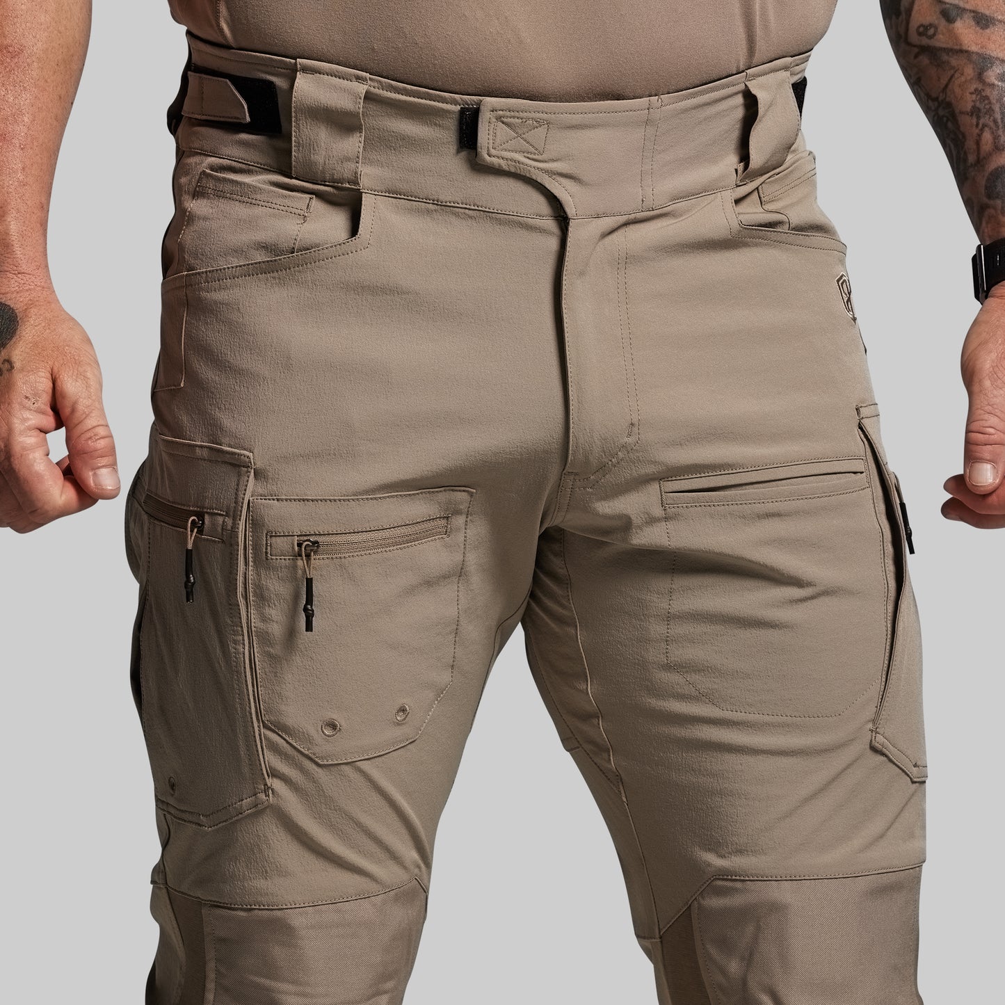 Tan tactical pants with multiple pockets on a plain background