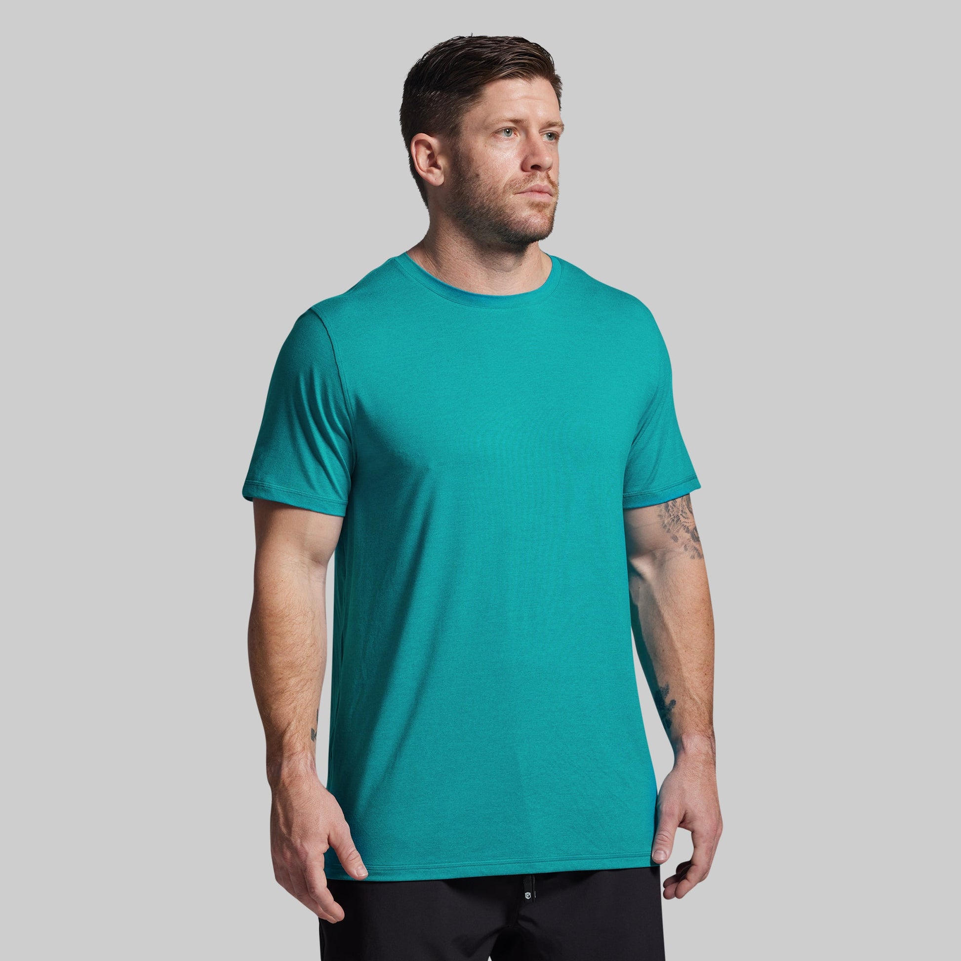 Man wearing a teal t-shirt against a gray background