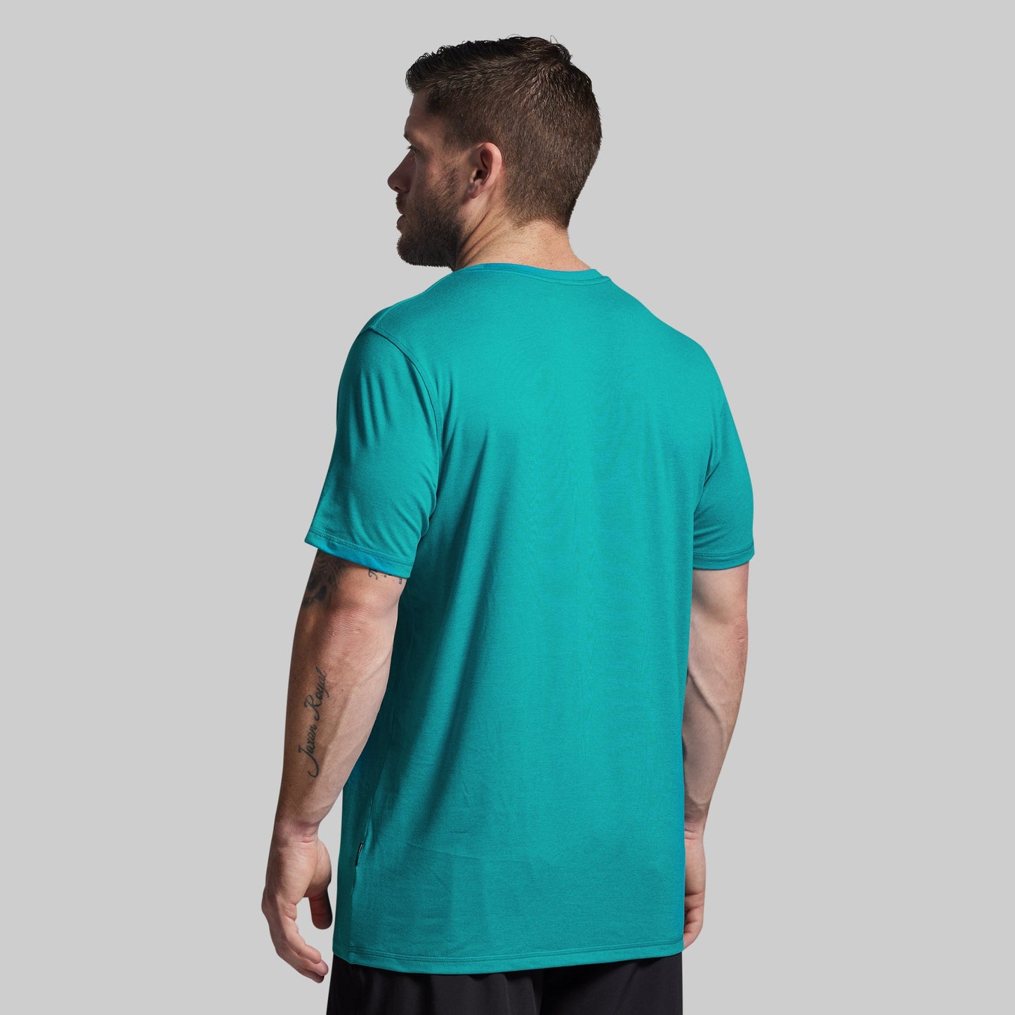 Man wearing a teal t-shirt on a gray background