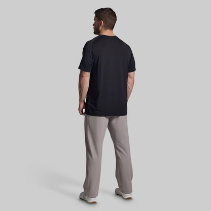 Man wearing a black t-shirt and gray pants on a light gray background