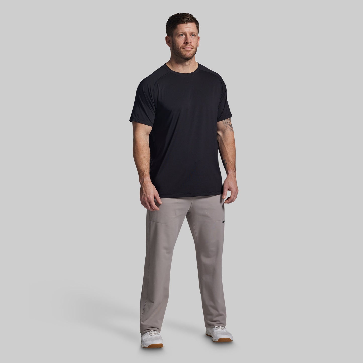 Man wearing a black t-shirt and gray pants on a light gray background