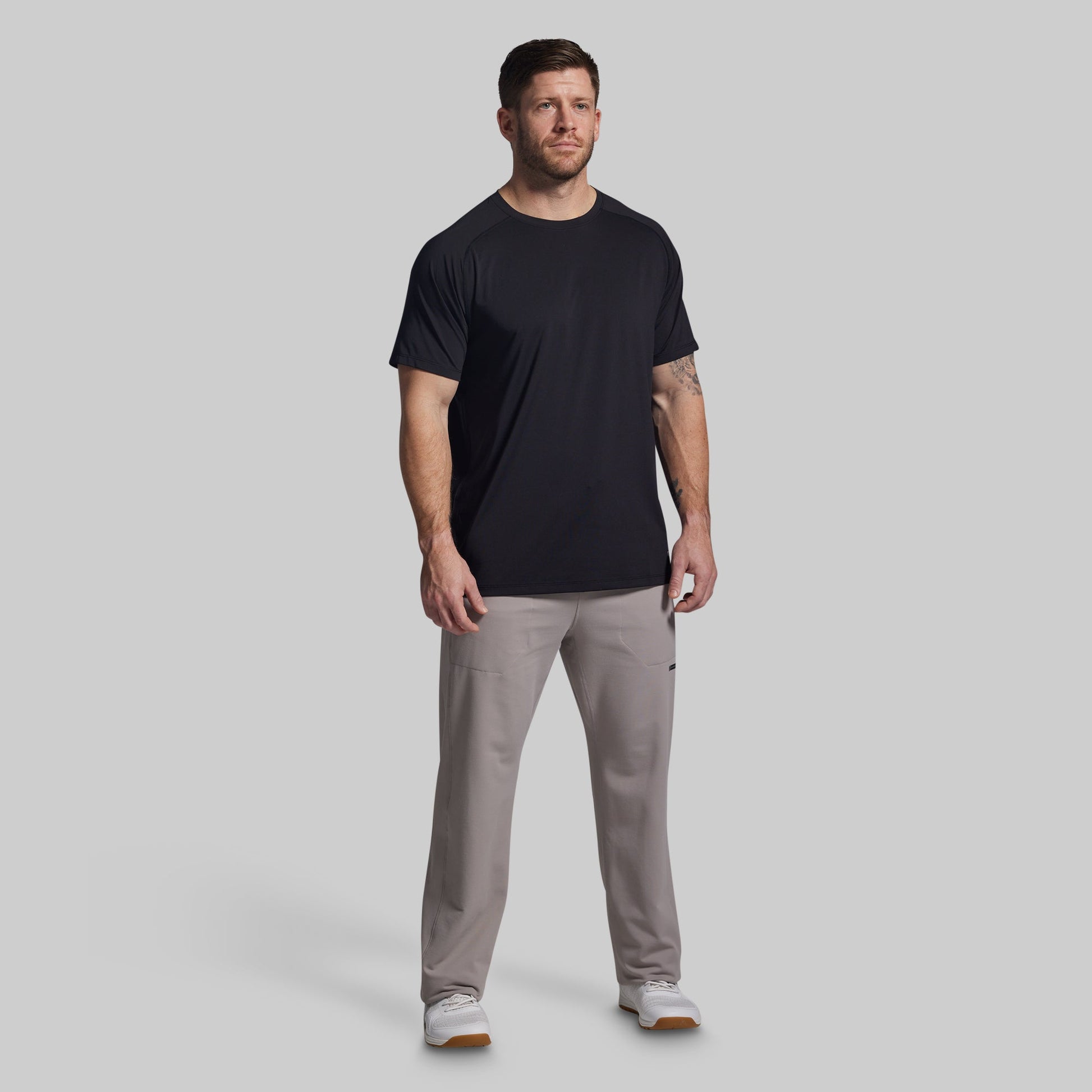 Man wearing a black t-shirt and gray pants on a light gray background