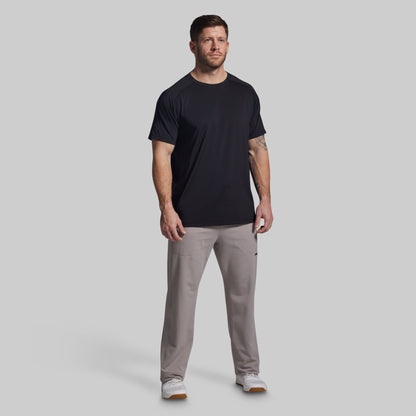 Man wearing a black t-shirt and gray pants on a light gray background