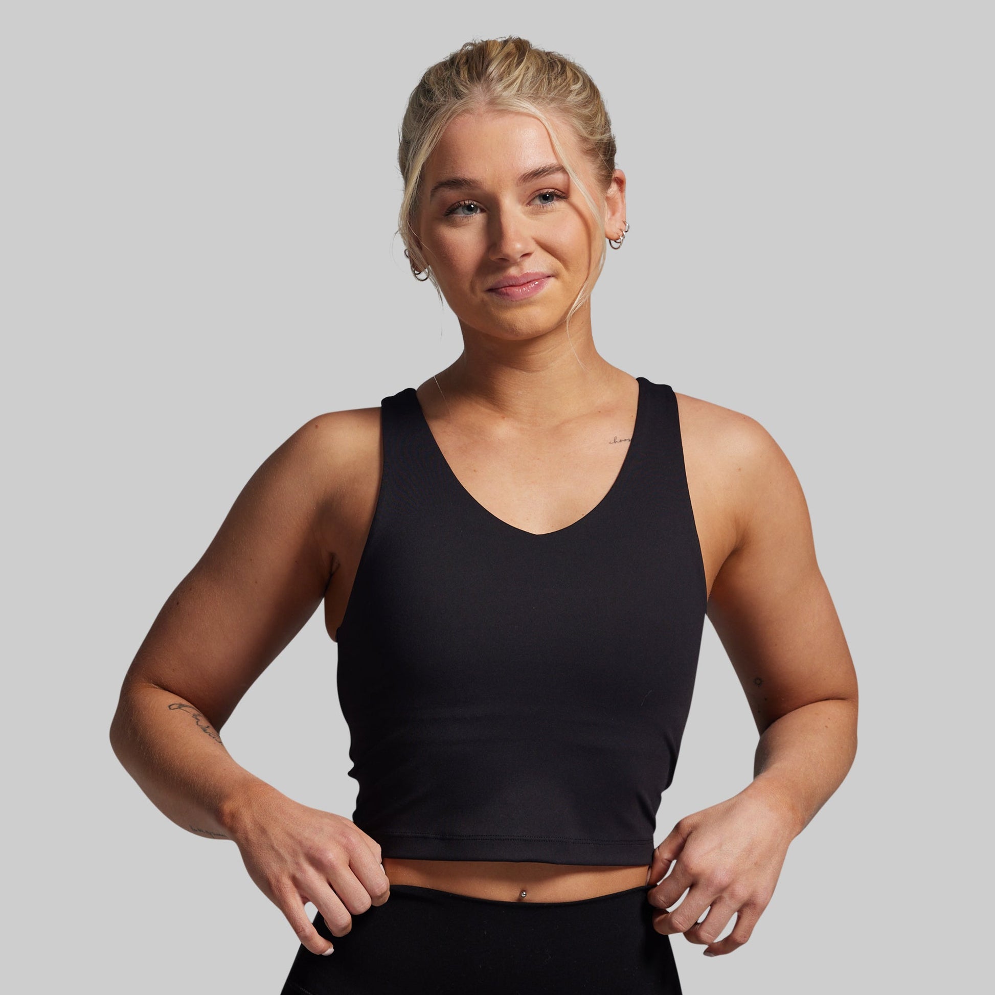Woman wearing a black tank top against a plain background