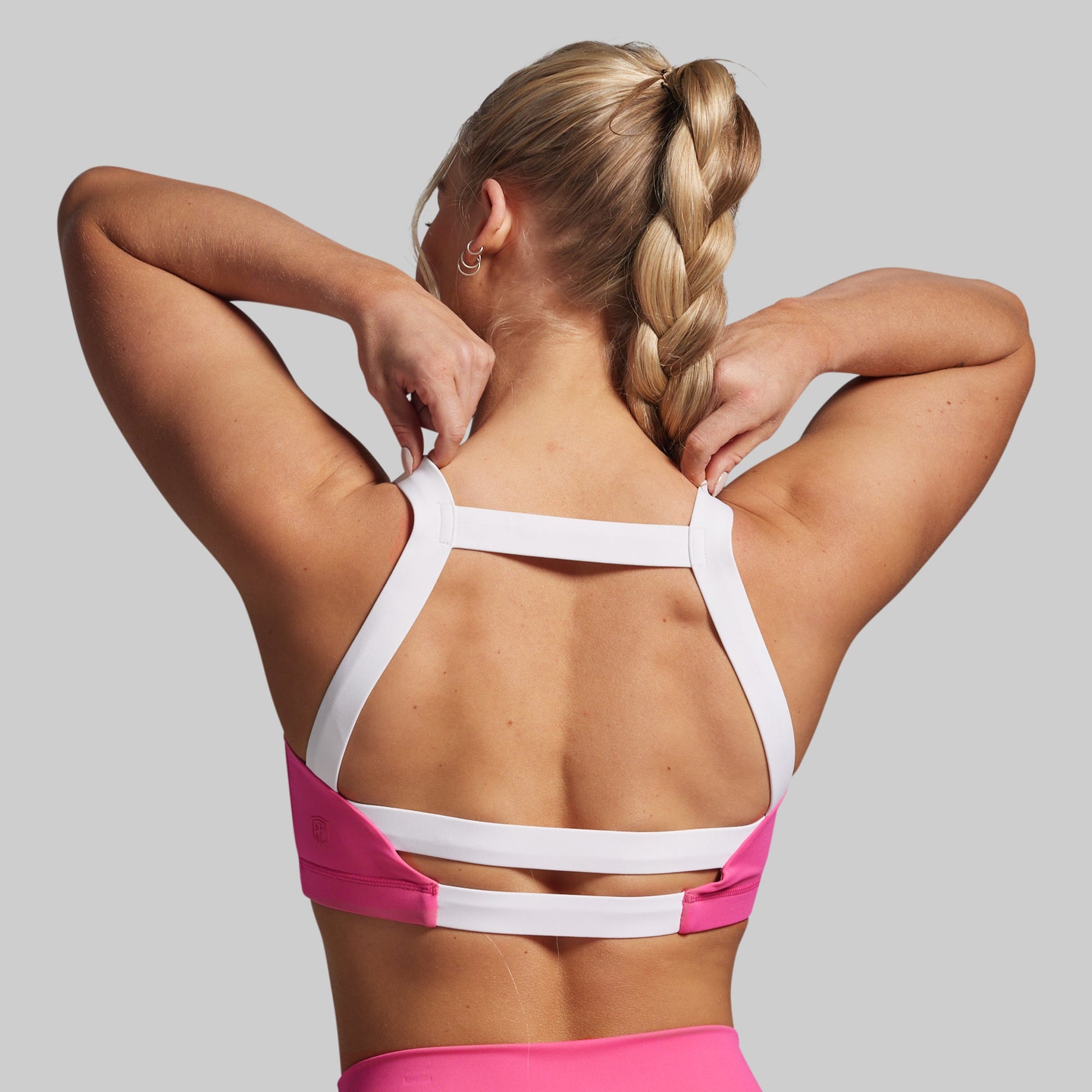 Woman wearing a pink and white sports bra on a gray background