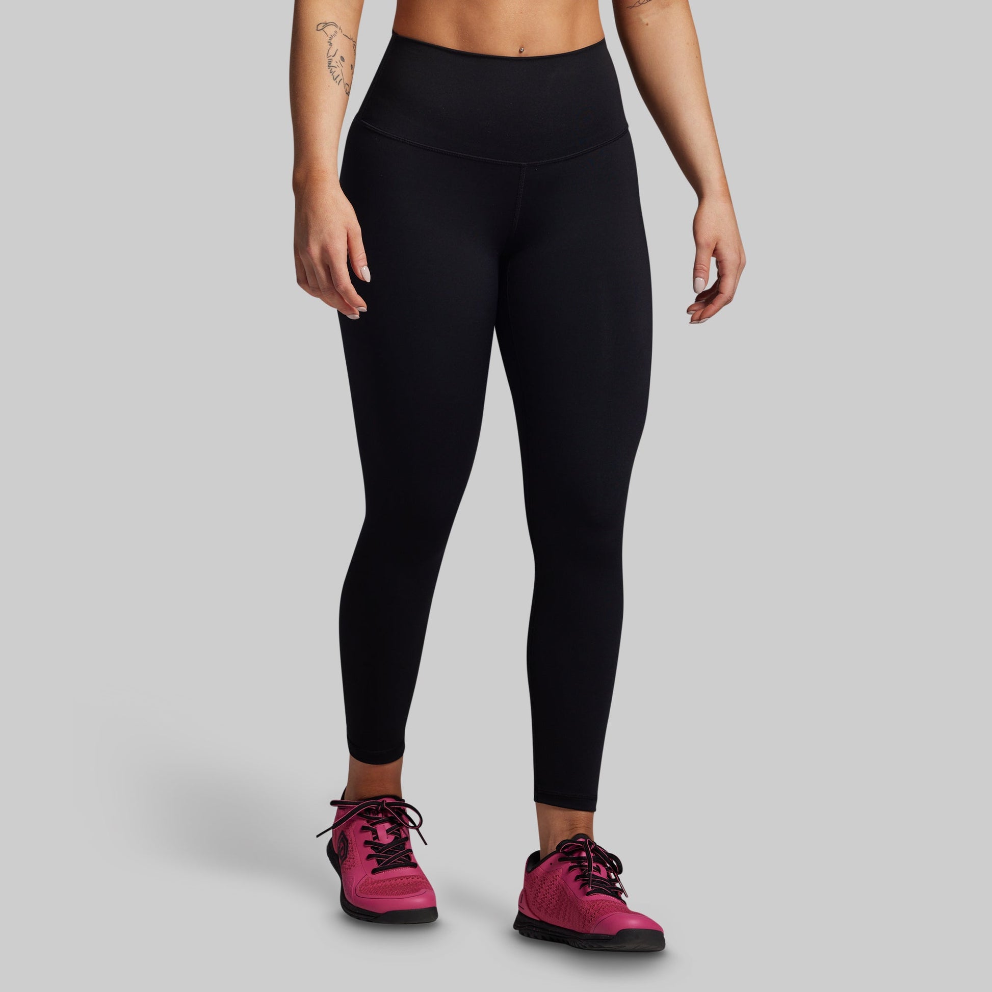 Person wearing black leggings and pink sneakers on a gray background