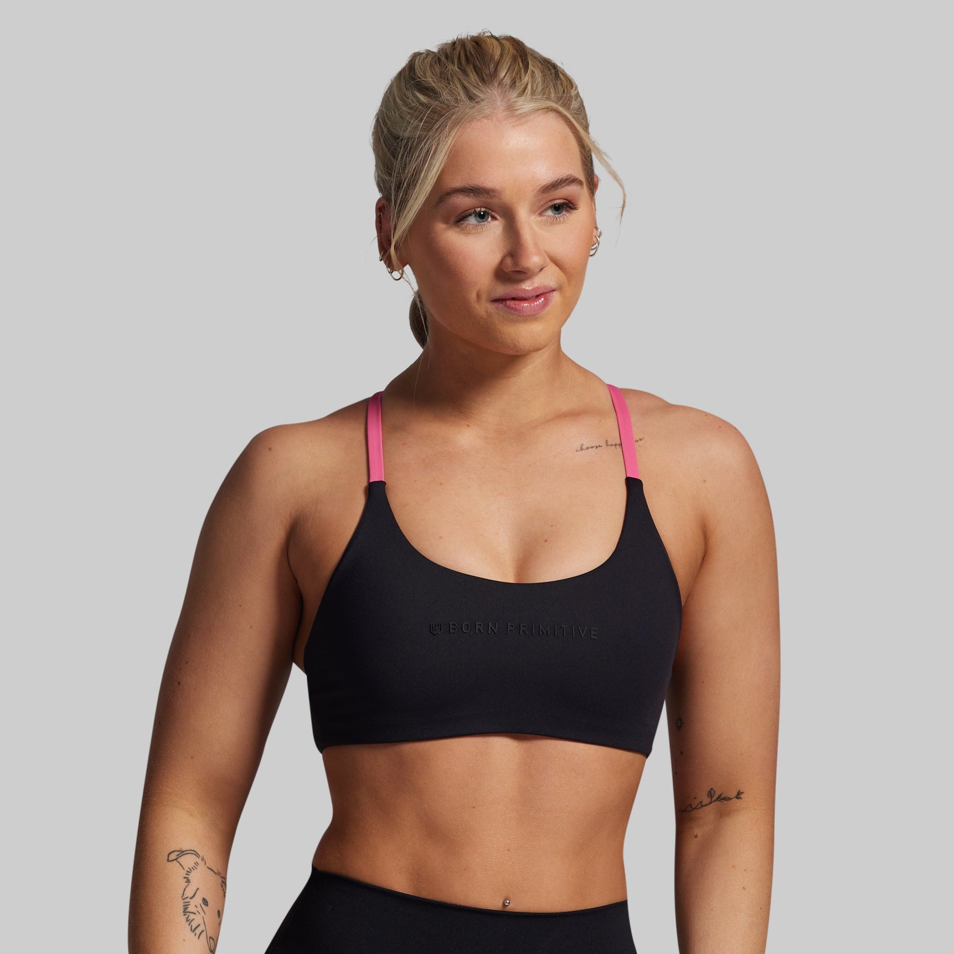 Woman wearing a black sports bra with pink straps on a gray background