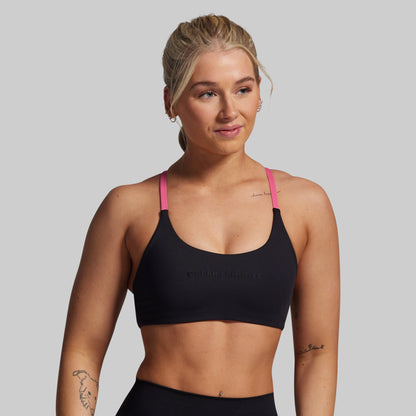 Woman wearing a black sports bra with pink straps on a gray background