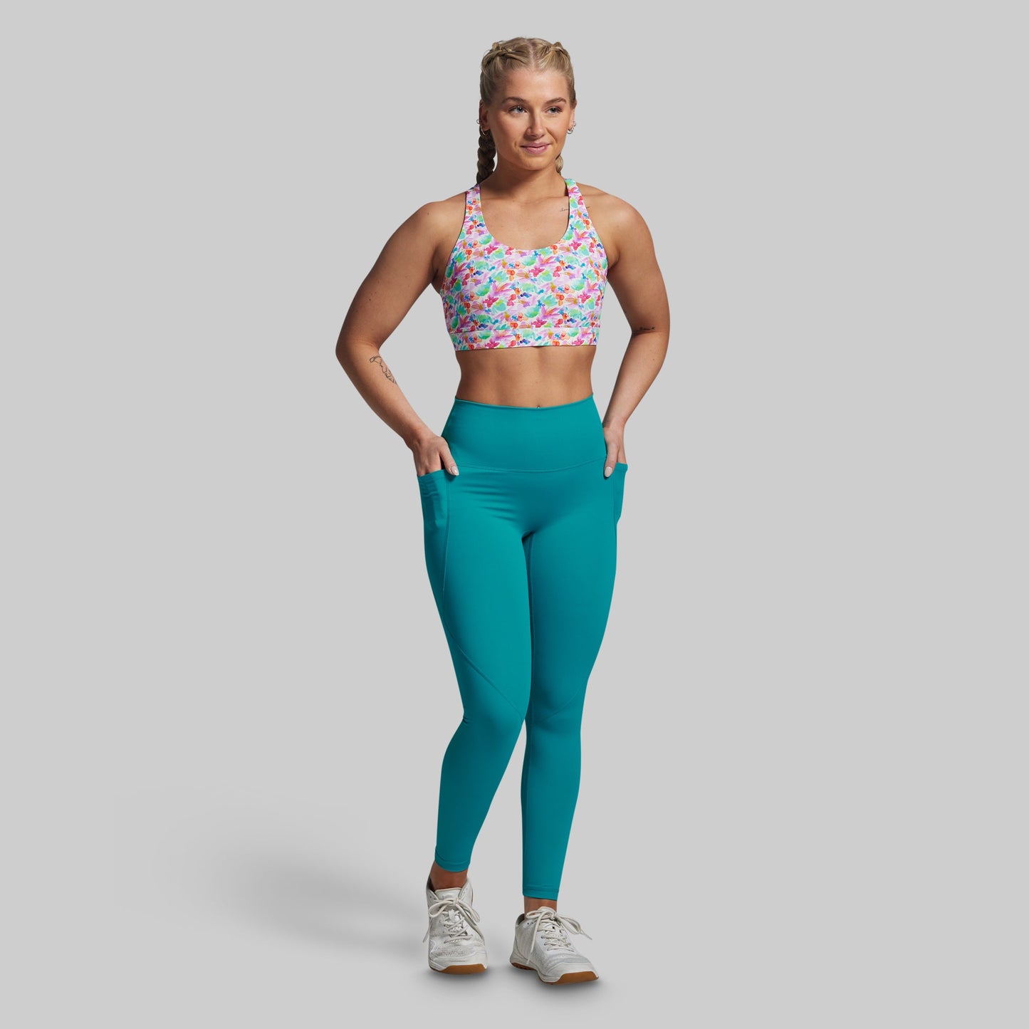 Woman wearing a colorful sports bra and teal leggings on a gray background