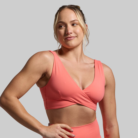 Woman wearing a coral sports bra and leggings on a gray background